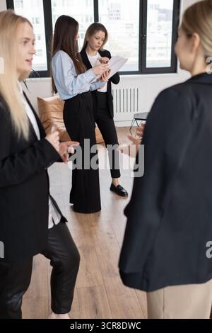 Vier Geschäftsfrauen versammelten sich während der Besprechung in modernen Büroumgebungen, zwei Fachleute analysierten Dokumente, während Kollegen sich unterhalten, Stockfoto