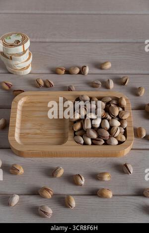 Blick von oben auf rustikale Pistazien auf einem Holztablett, verstreut auf einer hellen Holzoberfläche, die natürliche Texturen und Erdtöne hervorhebt Stockfoto