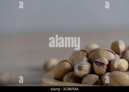 Blick von oben auf rustikale Pistazien auf einem Holztablett, verstreut auf einer hellen Holzoberfläche, die natürliche Texturen und Erdtöne hervorhebt Stockfoto