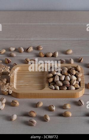 Blick von oben auf rustikale Pistazien auf einem Holztablett, verstreut auf einer hellen Holzoberfläche, die natürliche Texturen und Erdtöne hervorhebt Stockfoto