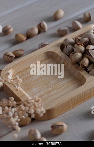 Blick von oben auf rustikale Pistazien auf einem Holztablett, verstreut auf einer hellen Holzoberfläche, die natürliche Texturen und Erdtöne hervorhebt Stockfoto