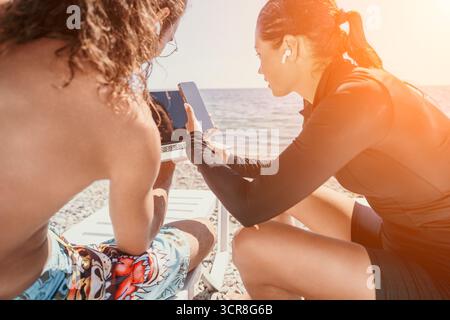 Segelpaar Tablet Ocean - zwei Personen auf einem Segelboot, die an einem sonnigen Tag auf ein Tablet schauen. Stockfoto