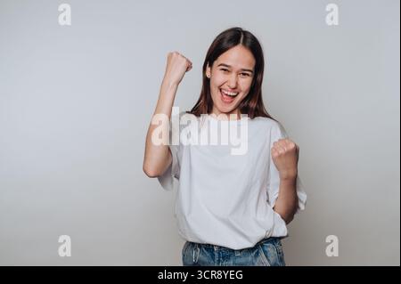 Junge asiatische Frau feiert Erfolg mit fröhlichem Ausdruck in lässigem Outfit vor neutralem Hintergrund Stockfoto
