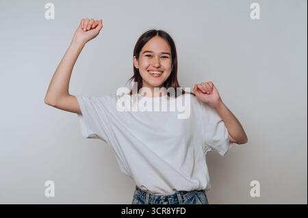 Die junge asiatische Frau tanzt tagsüber in lässiger Kleidung mit einem hellen, fröhlichen Ausdruck im Haus Stockfoto