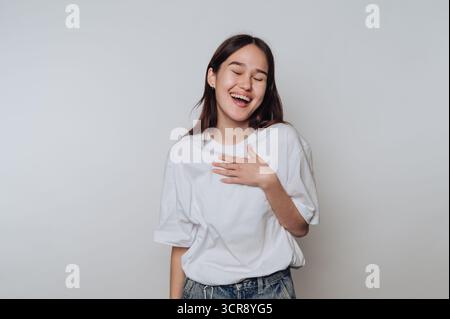 Die junge asiatische Frau genießt einen unbeschwerten Moment mit einem fröhlichen Ausdruck, während sie vor einem einfachen Hintergrund posiert Stockfoto