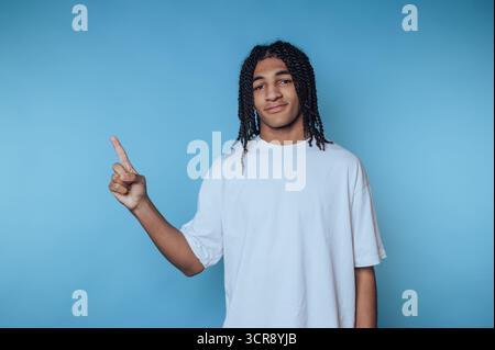 Teenager gibt positive Gesten, während sie in einem legeren Outfit drinnen vor einem durchsichtigen blauen Hintergrund stehen Stockfoto