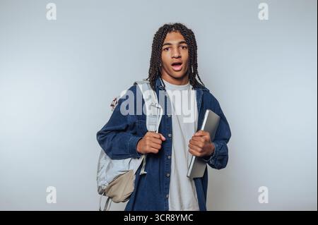 Der Schüler mit Rucksack und Laptop bringt seine Überraschung in ungezwungener Innenumgebung zum Ausdruck Stockfoto