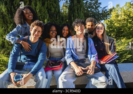 Eine vielfältige Gruppe glücklicher junger Studentinnen und Studenten, die draußen auf dem Campus sitzen und Freundschaft, Bildung und multikulturellen Kontakt aufnehmen Stockfoto