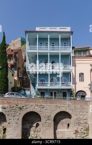 Der Blick auf ein dreistöckiges Gebäude mit hellblauen Wänden und weißen Balkonen steht über einem Steinbogen unter klarem Himmel, Abanotubani, Tiflis, Georgien. Stockfoto