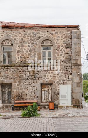 Blick auf ein Steingebäude mit Bogenfenstern und einer abgenutzten Bank, die an der strukturierten Fassade auf dem historischen Stadtplatz in Goris, Provinz Syunik, Armenien, ruht. Stockfoto