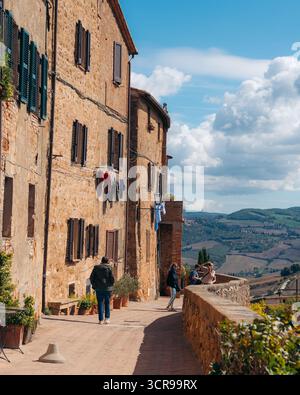 Blick auf rustikale Steinhäuser in der warmen toskanischen Sonne, die Kleidung hängt sanft, während die Menschen entlang des alten Pfades laufen, Pienza, Toskana, Italien. Stockfoto