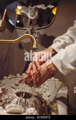 In einer ruhigen Umgebung reinigt eine junge Frau mit stilvollen Perlperlen in verschiedenen Formen ihre Hände an einem einzigartigen Waschtisch mit Muscheln und kreiert so Stockfoto