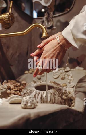 Eine junge Frau wäscht sich die Hände in einem dekorativen Waschtisch, der mit Muscheln verziert ist und modische Perlen in verschiedenen Formen zeigt. In diesem Moment Stockfoto