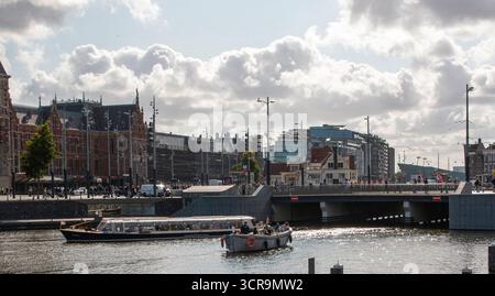 Amsterdam, Niederlande - 5. August 2025: Ein Boot gleitet durch ruhiges Wasser in der Nähe moderner Gebäude unter bewölktem Himmel. Stockfoto