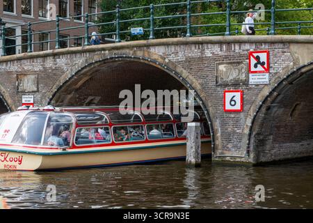 Amsterdam, Niederlande - 5. August 2025: Ein malerisches Boot gleitet durch Amsterdams historische Kanäle unter einer Steinbrücke. Stockfoto