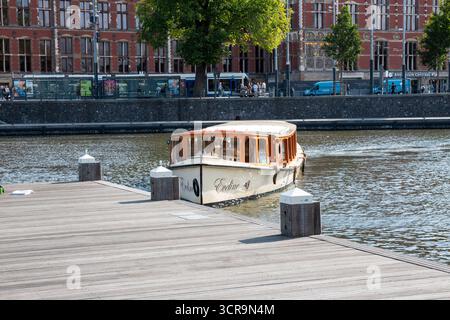 Amsterdam, Niederlande - 5. August 2025: Ein Boot gleitet sanft auf dem Fluss, umgeben von Gebäuden und Bäumen. Stockfoto