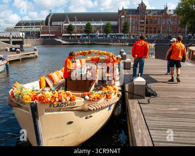 Amsterdam, Niederlande - 5. August 2025: Touristen steigen an einem belebten Ort am Wasser an Bord eines festlich geschmückten Bootes. Stockfoto