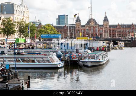 Amsterdam, Niederlande - 5. August 2025: Boote legen an einem lebhaften Yachthafen mit historischen Gebäuden in der Nähe an. Stockfoto