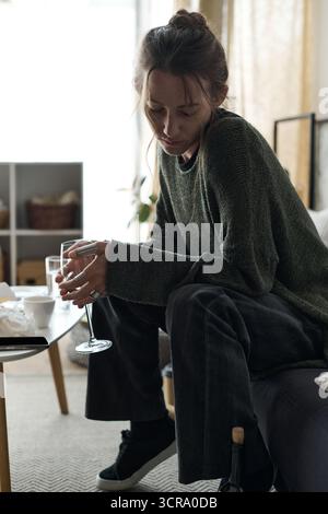 Eine junge Frau sitzt still auf ihrer Couch und fühlt zu Hause das Gewicht der Traurigkeit. Stockfoto