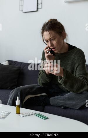 Eine junge Frau sitzt zu Hause auf ihrer Couch und fühlt sich beim Telefonieren überwältigt. Stockfoto