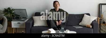Eine junge Frau sitzt leise auf einer Couch in ihrem Wohnzimmer und reflektiert ihre Gefühle in Einsamkeit. Stockfoto