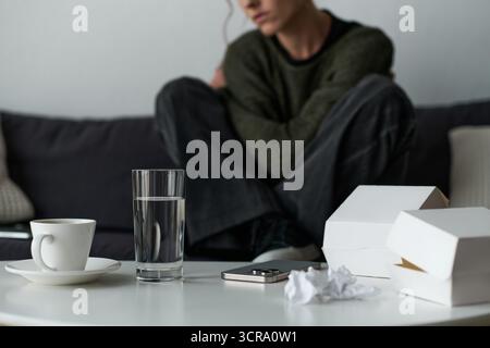 Eine junge Frau sitzt still auf einer Couch mit hochgezogenen Knien, verloren in ihren Gefühlen zu Hause. Stockfoto