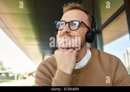 Ein junger Lehrer entspannt sich im Freien, trägt Kopfhörer und denkt an einem sonnigen Tag über Ideen nach. Stockfoto