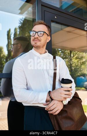 Ein junger Mann posiert selbstbewusst mit einer Kaffeetasse, während er sich gegen einen Glaseingang lehnt. Stockfoto