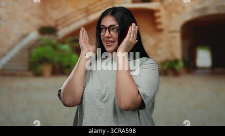 Die Frau, die im Freien in einer städtischen Straßenlage lächelt, zeigt Glück und Selbstvertrauen mit lässiger Kleidung und Brille, die einen charmanten Stil in Plus-Größe unterstreichen Stockfoto