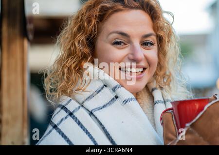 Rothaarige glückliche Frau trinkt Glühwein in roter Tasse auf dem Weihnachtsmarkt. Genießen Sie den Winterurlaub. Stockfoto