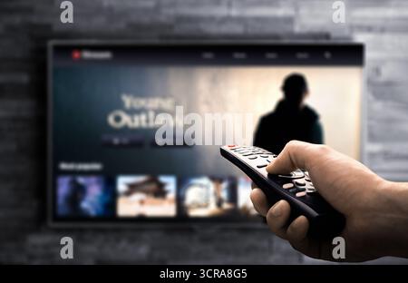 TV-Stream nach Hause. Sehen Sie sich echte Krimi-Filme oder -Serien nachts auf dem Fernsehbildschirm an. Remote-pov in Hand. Mockup der Videoplattform. Stockfoto