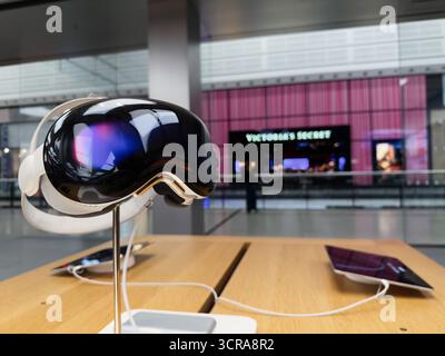 Manchester, Großbritannien – 29. September 2025: VR-Headset Apple Vision Pro auf einem Holztisch in einem modernen Einkaufszentrum mit einer pinkfarbenen Victoria's Secret-Ladenfront Stockfoto