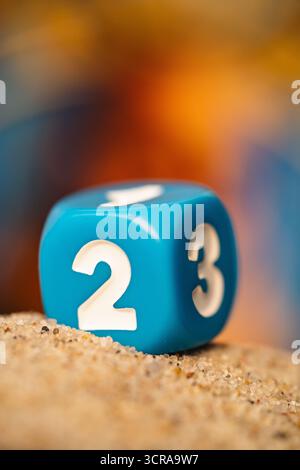 Makro-Nahaufnahme eines blauen benutzerdefinierten Würfels mit weißen Zahlen aus dem Brettspiel Camel Up, der auf Sand ruht mit geringer Schärfentiefe. Stockfoto
