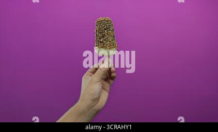 Kaukasischer Mann, der Eis mit Schokolade auf rosa Hintergrund hält, mit einer Hand isoliert in Studio-Beleuchtung für Dessert-Konzept Stockfoto