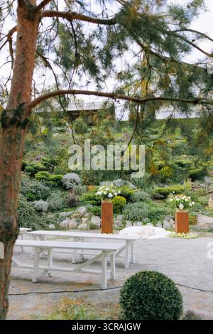 Hochzeitszeremonie im Freien mit Reihen weißer Holzbänke gegenüber zwei Podesten, die mit weißen Blumenarrangements und frischen Äpfeln dekoriert sind Stockfoto