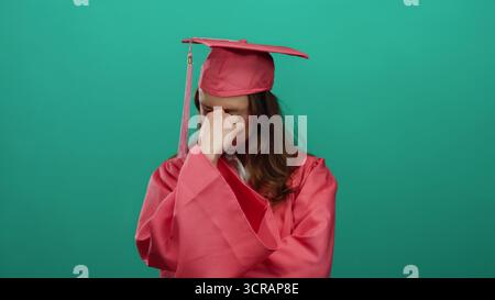 Frau im rosa Abschlusskleid, die über grünem Hintergrund steht, sieht nachdenklich und besinnlich aus und symbolisiert die Introspektion eines jungen Schülers auf Achiev Stockfoto