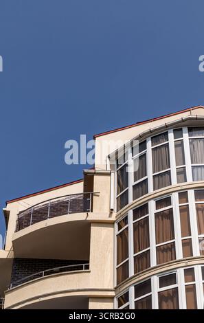 Teil der Fassade eines modernen Hotelgebäudes mit großen Glasfenstern und stilvollen halbrunden Balkonen vor dem blauen Himmel. Urbane Architektur Stockfoto