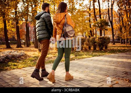 Ein Paar genießt einen romantischen Herbstspaziergang in einem Park inmitten von Herbstlaub unter warmem Sonnenlicht und fängt einen ruhigen und liebevollen Moment ein Stockfoto