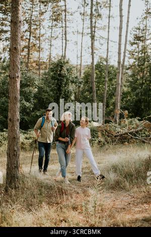 Eine Familie genießt eine gemütliche Wanderung in einer ruhigen Waldlandschaft, umgeben von hohen Bäumen und Grün. Sie teilen Lachen und Momente, während sie Th erkunden Stockfoto