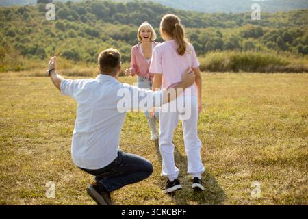 Eine Familie genießt einen sonnigen Tag im Freien auf einer Wiese. Zwei Individuen nehmen den freudigen Moment wahr, während ein Kind eifrig auf sie zuläuft und ein glückliches Ich erschafft Stockfoto