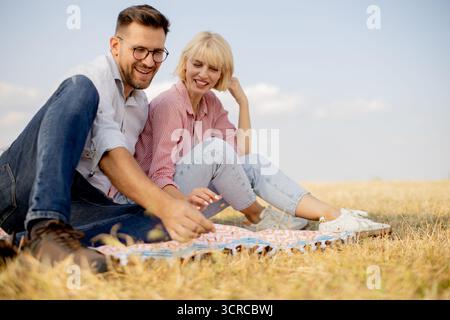 Zwei Freunde entspannen sich auf einer Picknickdecke und teilen sich Lachen und gute Stimmung unter hellem Himmel auf einem goldenen Grasfeld. Stockfoto