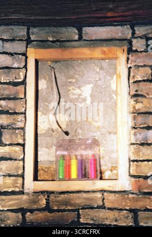 Bunte Stifte, die in einem Holzrahmen gegen eine Ziegelwand arrangiert sind, gestylt als warmes zeitgenössisches Interieur mit analoger Filmästhetik. Stockfoto