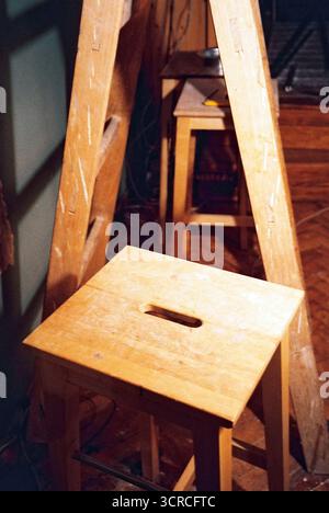 Natürliche Holzbarhocker und eine Leiter in einem Apartmentzimmer in Renovierung, umgeben von unfertigen Oberflächen und Baudetails, Analogfilm. Stockfoto