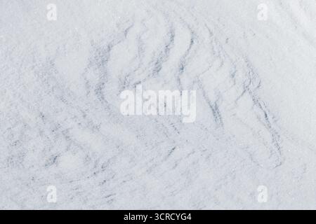 Die Reliefschneeoberfläche mit blassblauen Schatten schafft eine ruhige, winterliche Kulisse, die sich für saisonale Designs, Begrüßungen oder Produktmodelle eignet. Ideal für unterwegs Stockfoto