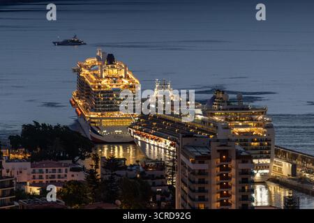 Die beleuchteten P&O-Kreuzfahrtschiffe Iona & Ventura legen während der Dämmerung im Hafen von Funchal an, mit Blick auf die städtische Küstenlandschaft und das ruhige Wasser Stockfoto