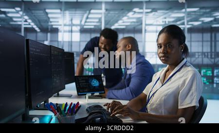 Teamleiter im Serverraum unterrichtet den Praktikanten bei der Entwicklung von Disaster Recovery-Plänen, die minimale Ausfallzeiten gewährleisten. IT-Spezialist für Rechenzentren, der Mitarbeiter bei der Leistungsüberwachung unterstützt, Kamera A Stockfoto