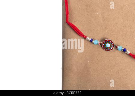 Ein leuchtendes Perlenarmband mit rundem Medaillon in der Mitte und roter Kordel auf Kraftpapier, das farbenfrohe türkisfarbene, blaue und silberne Perlen zeigt. Stockfoto
