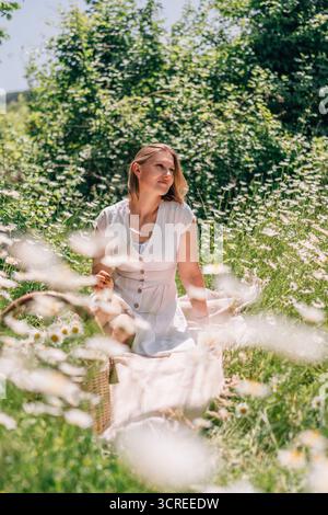 Daisy Picnic Woman Summer: Frau sitzt im Sommer zwischen Gänseblümchen auf einem Feld für ein Picknick. Stockfoto