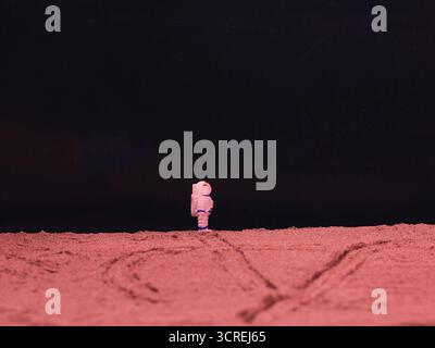 Dieses Bild zeigt einen Astronauten, der auf einer roten Oberfläche steht, die dem Mars oder dem Mond ähnelt. Reifenspuren sind auf dem Sand sichtbar. Stockfoto