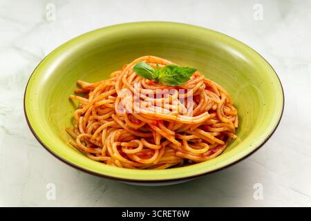 Italienische Spaghetti-Pasta in einer grünen Schüssel, belegt mit frischem Basilikumblatt Stockfoto